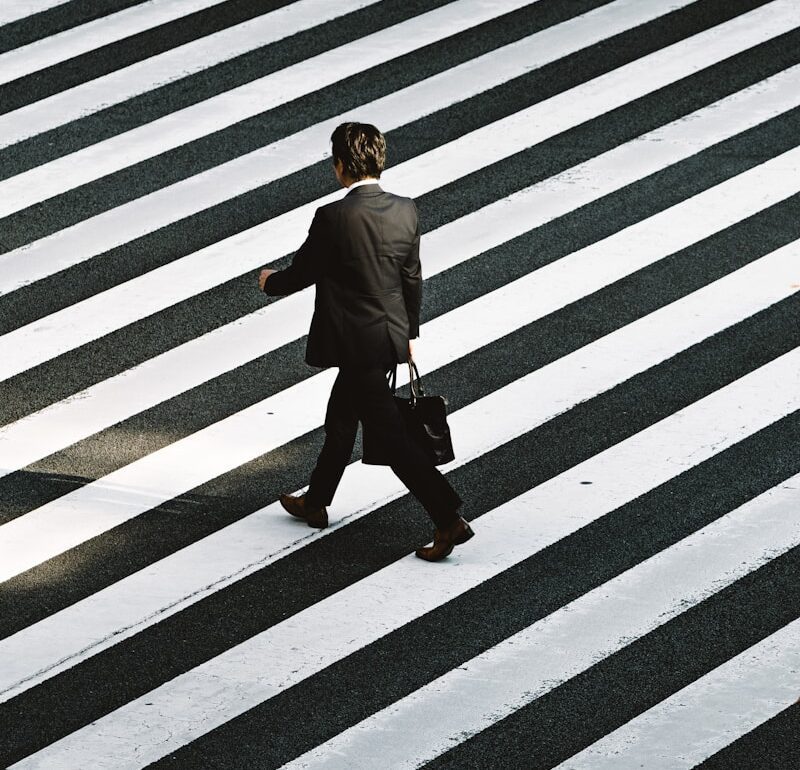 man in black formal suit jacket and pants carrying black bag while walking on pedestrian lane during daytime