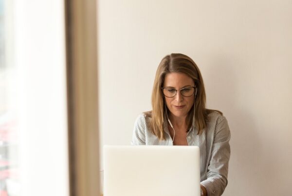 woman wearing grey striped dress shirt sitting down near brown wooden table in front of white laptop computer