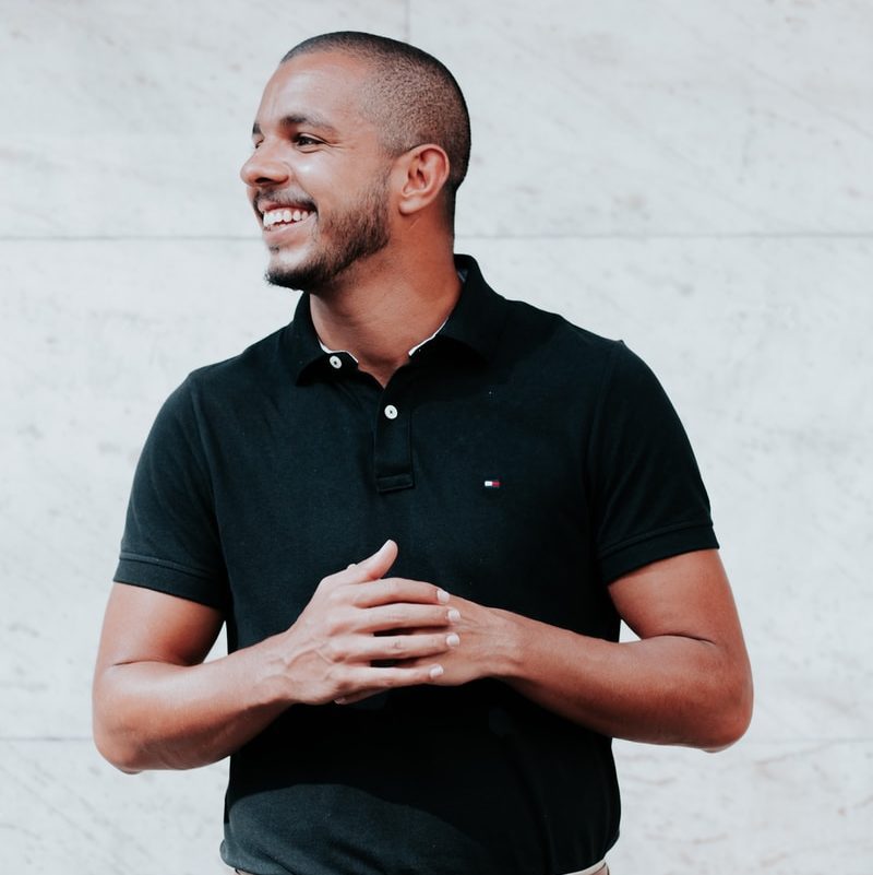 man in black polo shirt standing near white wall